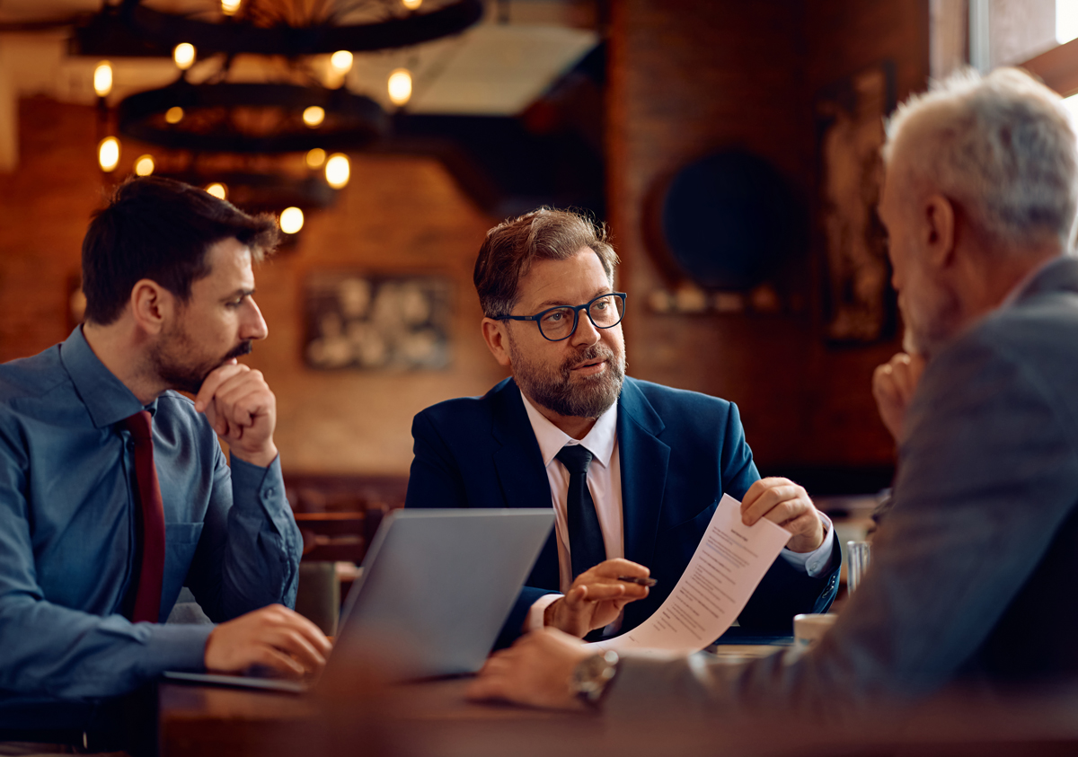 Mature businessman and his colleagues going through reports during a meeting in a cafe.